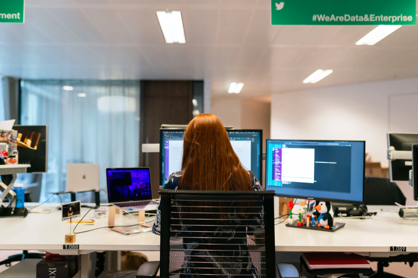 a data professional sits at her desk with two computer monitors displaying code