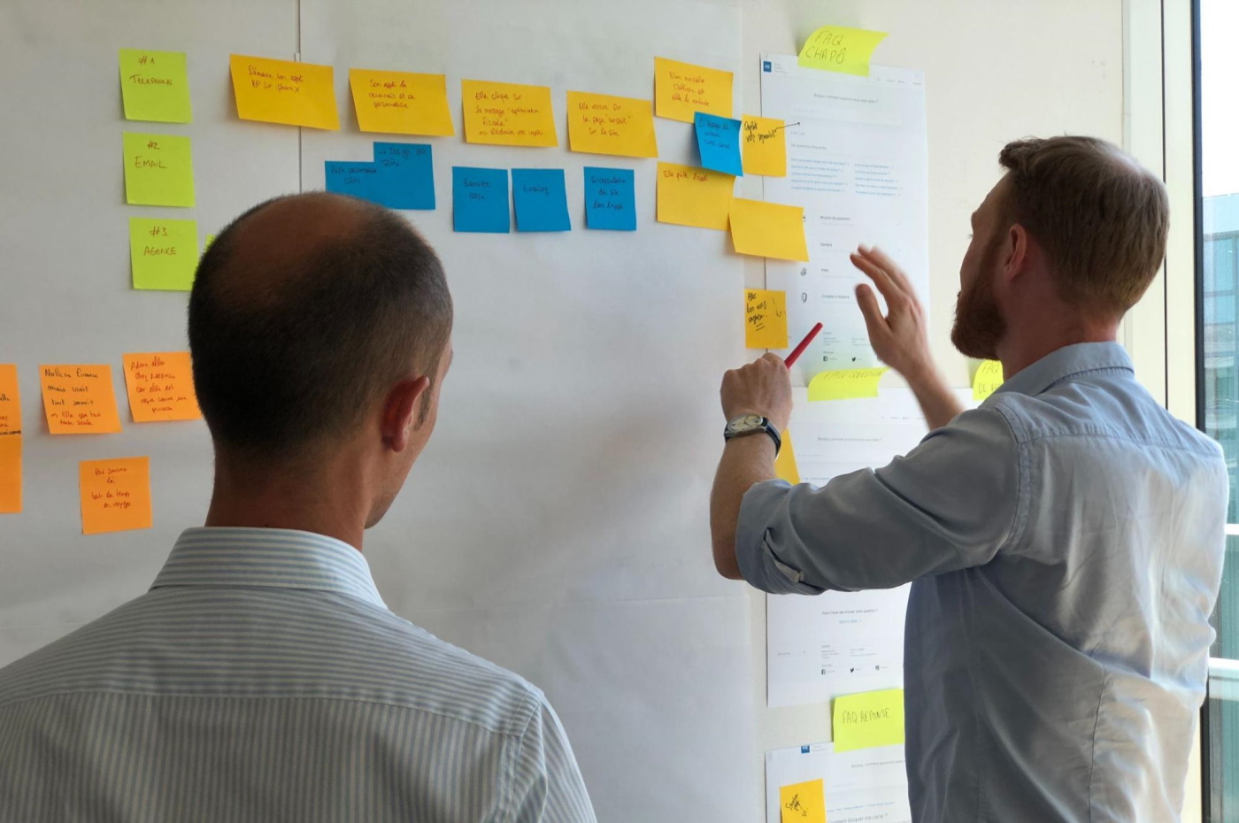 Two developers organize sticky notes on a wall to plan the layout of a program built with a no-code platform.