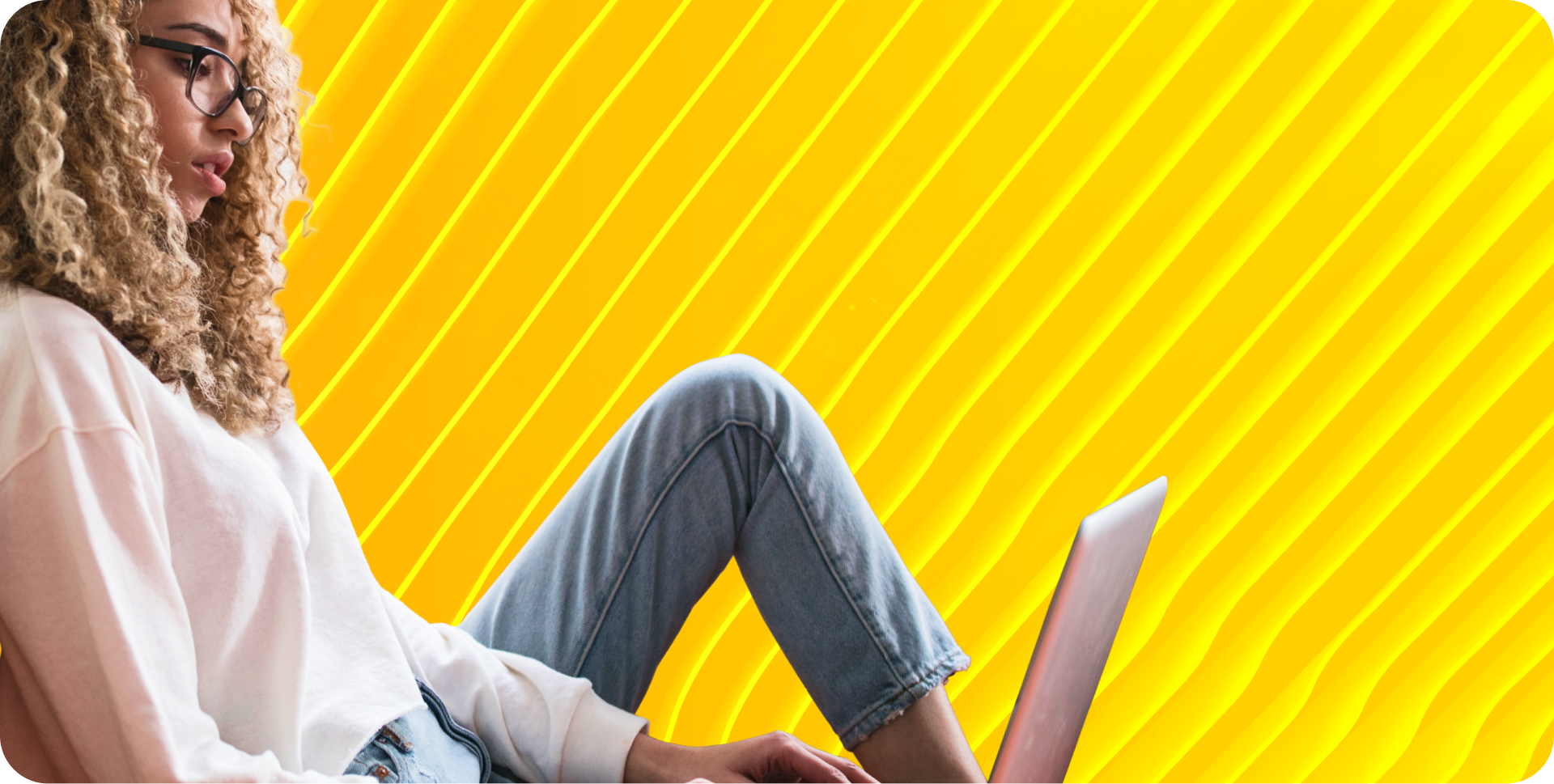 DevOps engineer sits with one leg folded while looking down at her laptop.