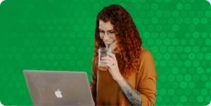 A DevOps engineer works at her laptop while smiling and drinking from an iced coffee with a straw.