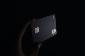 Close-up of a hand holding a matte black credit card in front of a dark background.