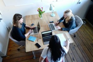 Three coworkers sit around a table each working on a laptop.