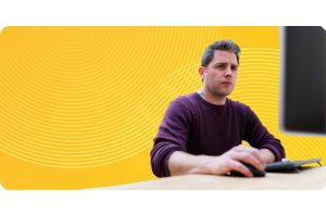 A CTO sits at a desktop with his hand resting on the mouse in the foreground of a bright yellow spiral background.