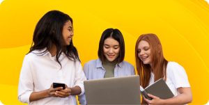 Three engineers stand together and look toward the engineer in the center holding a laptop.