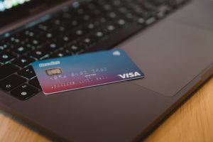 A blue and purple ombre Visa credit card sits on a keyboard laptop.