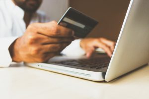 A man holds his credit card up to input the info on a laptop computer.