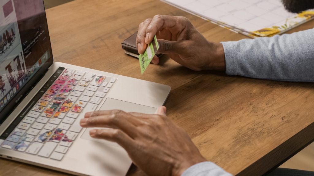 A man holds a lime green credit card in one hand and uses a MacBook Pro trackpad with the other.