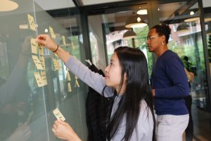 Woman removing sticky notes from Q1 column on a Kanban board while her teammate observes in the background.