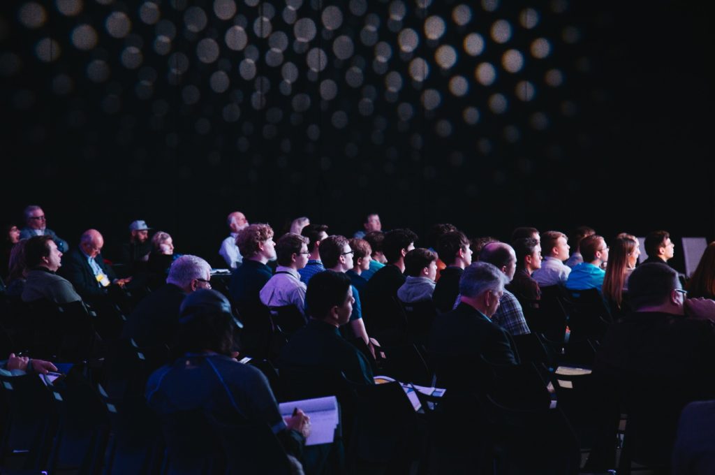 A crowd of people watches a presentation at a conference