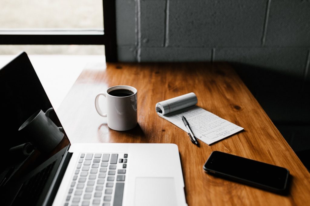 A laptop rests on a desk next to a smartphone, coffee mug, and notepad with a cloud migration checklist written down.