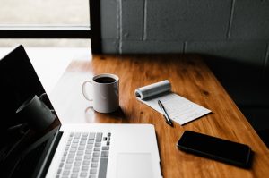 A laptop rests on a desk next to a smartphone, coffee mug, and notepad with a cloud migration checklist written down.