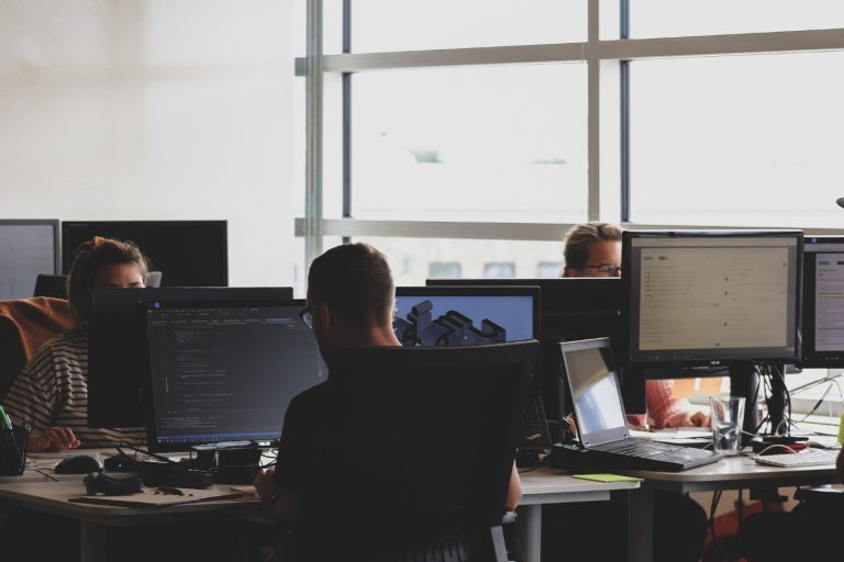 Workers in an office, sitting at a desk in front of a computer.