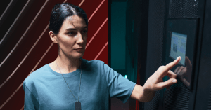 A woman holding a tablet in her right hand while tapping a screen on the wall with her left.