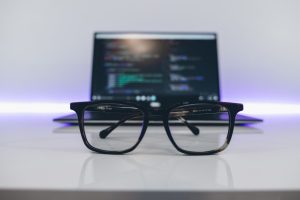 A pair of glasses rest in front of an open laptop.