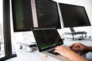 Engineer sitting in front of three computer screens filled with code.